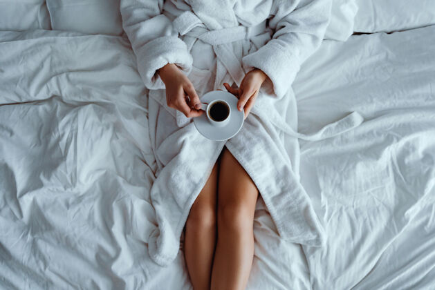 享受懒女人穿着浴衣躺在床上 享受着芳香的咖啡杯 在酒店舒适的卧室里放松房子醒来手