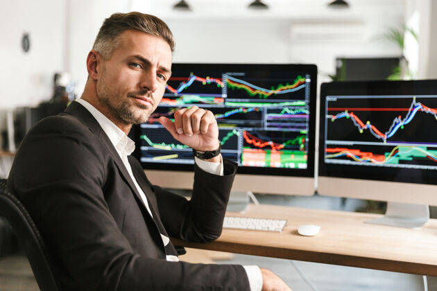 财务一张30多岁的现代商人穿着西装在电脑上工作的照片 屏幕上有图形和图表统计监视器主管
