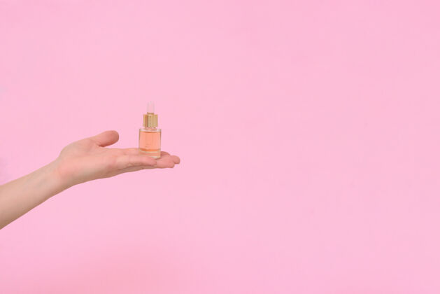 皮肤护理化妆品血清在透明玻璃滴管瓶在粉红色的背景在一个女人的手天然护肤品的概念精华护肤品 美丽健康肌肤产品健康乳液
