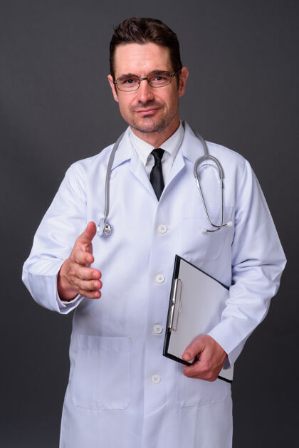 检查表长着胡子的帅哥医生戴着眼镜靠着灰墙眼镜协议听诊器