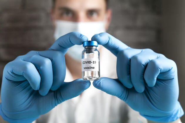 肺炎研究人员手里拿着Covid-19疫苗 男医生穿着白大褂 戴着医用口罩 戴着蓝色手套 手里拿着装有治疗冠状病毒疫苗的注射器和瓶子冠状病毒治疗的概念持有液体临床