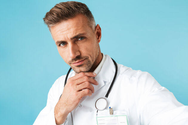 东西一张带听诊器的成熟医生独自站在蓝色墙壁上自拍的照片听诊器从业者肖像