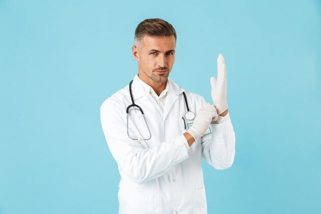 工人英俊的医生戴着听诊器戴着手套 孤立地站在蓝色的墙上医生肖像成熟