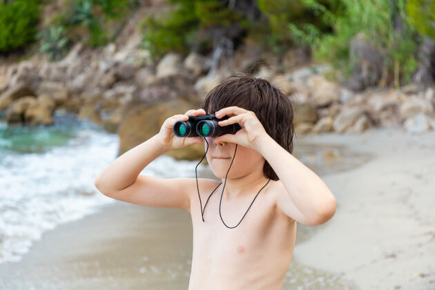 年轻一个小男孩呆在海边的海滩上 用望远镜看东西男孩水沙子