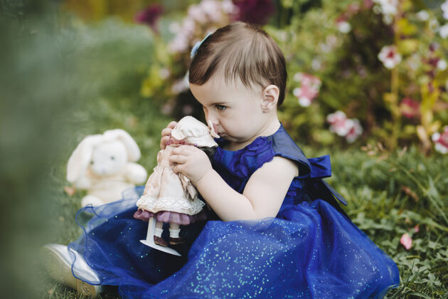 休闲可爱的小女孩抱着她的玩具和鼻子 坐在花园的草地上玩具快乐快乐