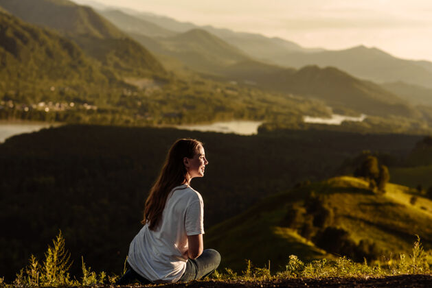 年轻快乐的年轻女游客坐在山谷和河流的背景下微笑着山女性自然