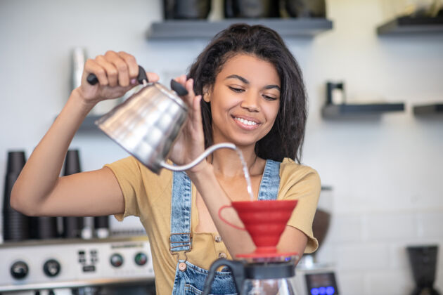 咖啡馆煮咖啡 咖啡师漂亮一个留着深色卷发的年轻女子 手里拿着茶壶在倒水自营职业咖啡师腰向上