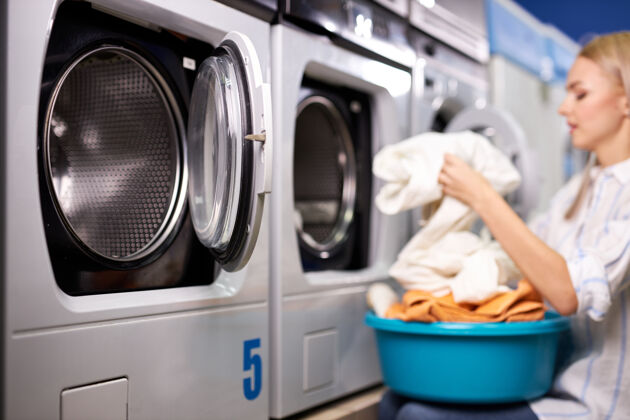 日常事务做家务的女人-洗衣房.女把干净的衣服叠在洗衣篮里 一边视图.清洁 清洗概念.焦点在洗衣机上脏洗衣家庭