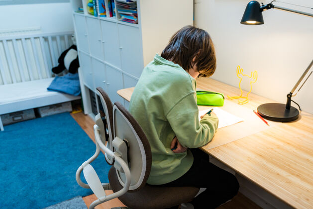 教育一个年轻的男生坐在手术台的矫形椅上做作业家集中儿童写作家庭教育概念小学生童年人