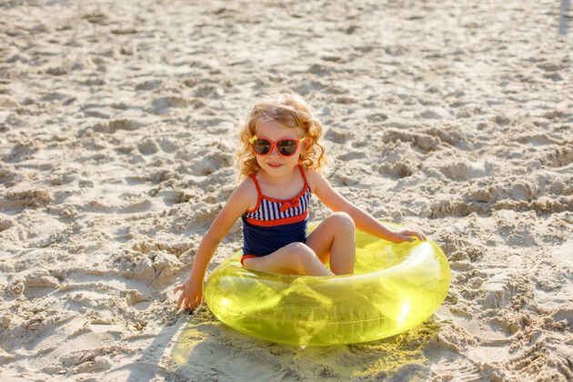 泳衣夏日沙滩上 戴着太阳镜的小女孩坐在充气圈上海洋大海太阳