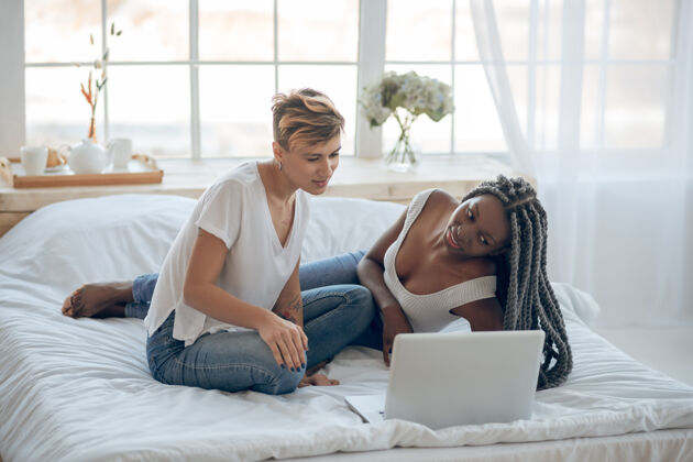 短发休闲2女孩们在笔记本电脑上看电影 感觉很积极非裔美国人连接长发