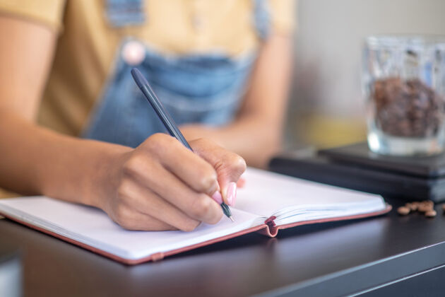 记事本女会计纤细优雅的手写体 用钢笔在笔记本的重量咖啡豆的柜台上秤咖啡馆手指