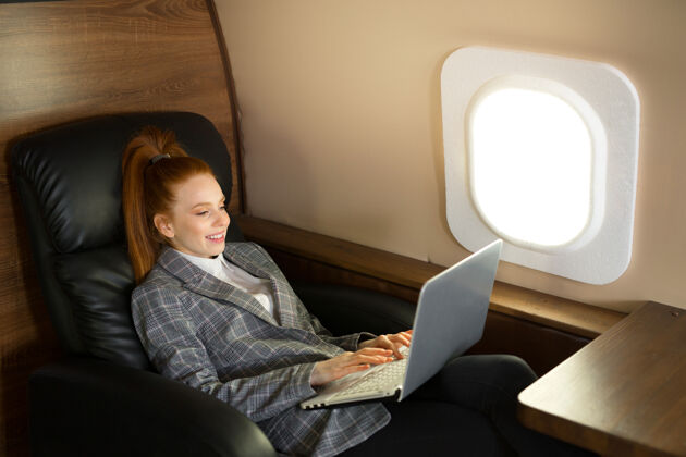 自信一位红发美女在机舱里拿着笔记本电脑舒适飞机飞行