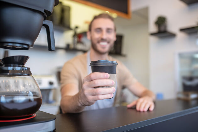 咖啡豆咖啡 心情.玻璃站在吧台后面微笑着的年轻咖啡师伸出手来品尝美味的新鲜咖啡咖啡馆咖啡壶创业
