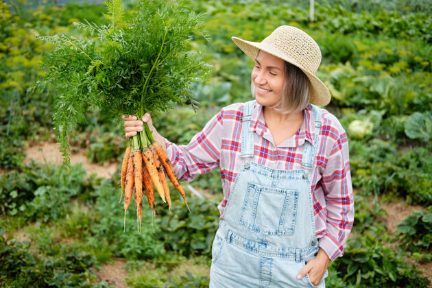 废物戴着帽子的可爱女孩在花园里摘胡萝卜花园.秋天蔬菜收获多种循环杂货