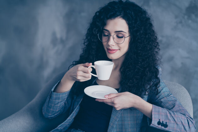 眼镜卷发女经理坐在椅子上喝着热咖啡隔着水泥墙椅子休息办公室