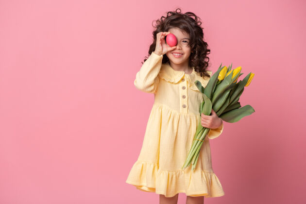 有趣有趣的小女孩拿着郁金香和五颜六色的复活节彩蛋在她眼前的粉红色背景女孩惊喜节日