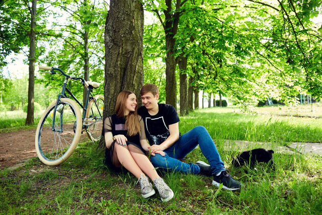 绿色一对相爱的情侣在公园的草地上的树旁休息快乐年轻欢呼