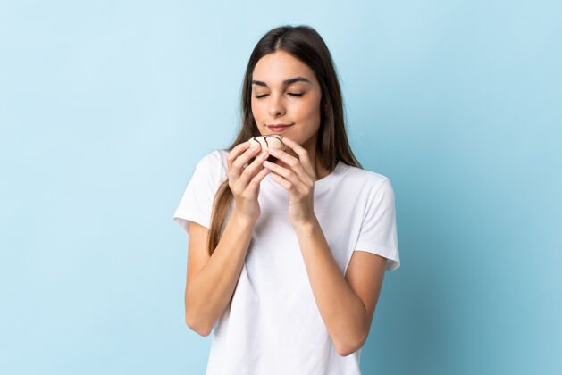 卡路里一个年轻的高加索女人拿着一个甜甜圈 被隔离在蓝色背景下女性甜美味