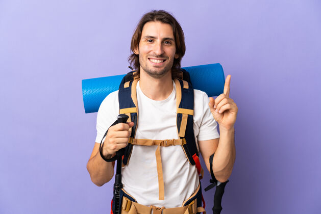 冒险一个年轻的登山者背着一个大背包翻过孤零零的墙 举起一个手指 表示最好的模型手势第一