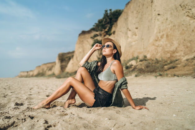 短裤戴帽子的黑发女孩在沙滩上和岩石一起放松女人户外太阳镜