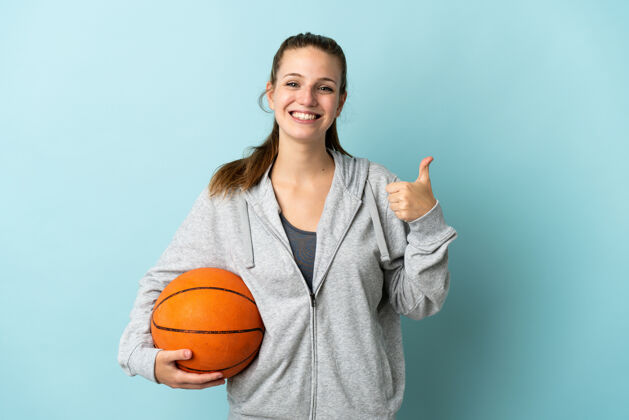 女孩一个年轻的白人女子 孤零零地站在蓝色背景下打篮球 竖起大拇指女人休闲成人