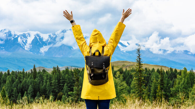 游客年轻的女游客举起双臂背着背包站在雪山的背景上山女人背包