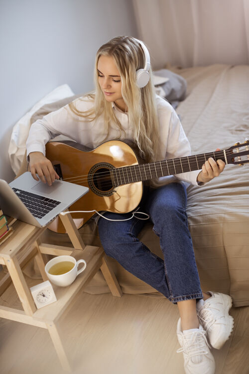 室内美丽的年轻女子坐在床上弹吉他主页.肖像可爱的女孩女孩美丽青少年