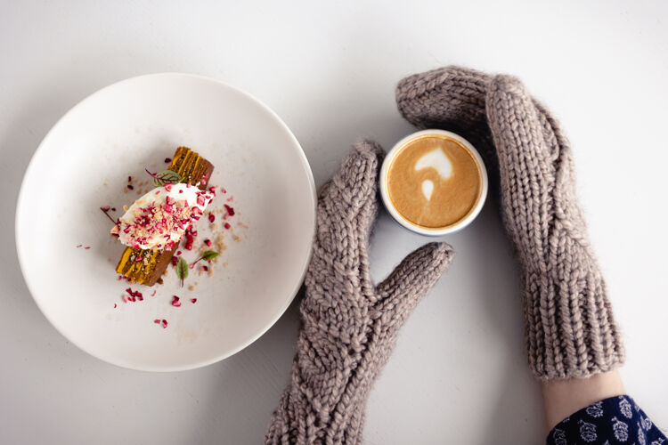 圣诞节一张白色的桌子上 一双棕色手套的女人手拿着一个咖啡杯和一个蛋糕冷羊毛美丽