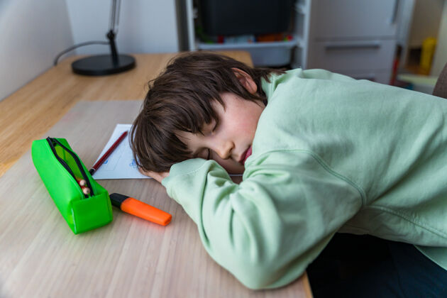 房子十岁的小男孩坐在桌子旁做作业回家累了孩子睡觉的时候在课桌上做运动学生孤独小学生