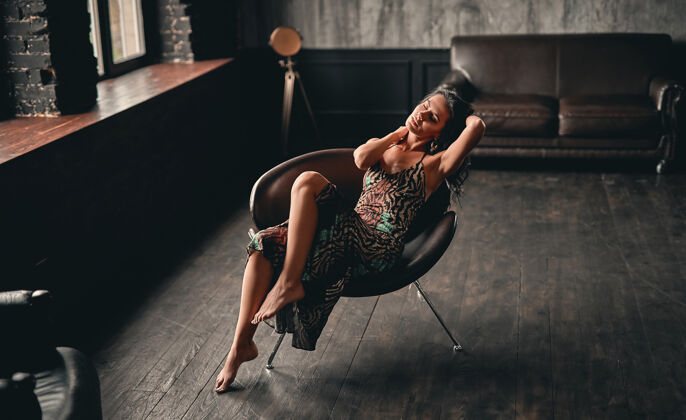 年轻一个漂亮的黑发女人的肖像 穿着裙子 坐在扶手椅上摆姿势 展现出美丽的修长双腿精致模特奢华