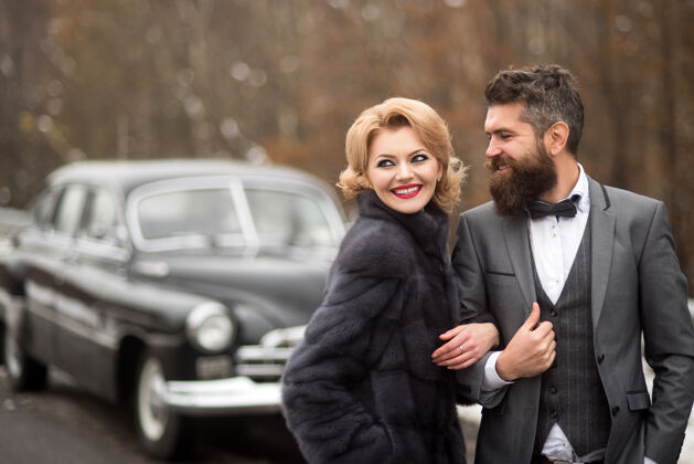 户外穿着黑色西装的新郎和女人在户外接近复古车浪漫日期.年份人近年轻夫妇公路旅行