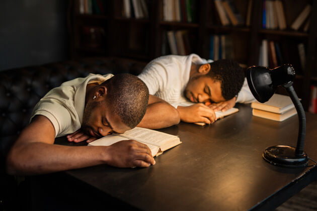 睡眠两个年轻的非洲男人正坐在一张桌子旁看书成功文学阅读