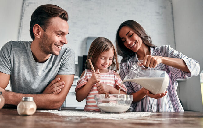 享受可爱的小女孩和她美丽的父母在厨房里揉面粉烤面包 一边微笑着做饭微笑面包房年轻
