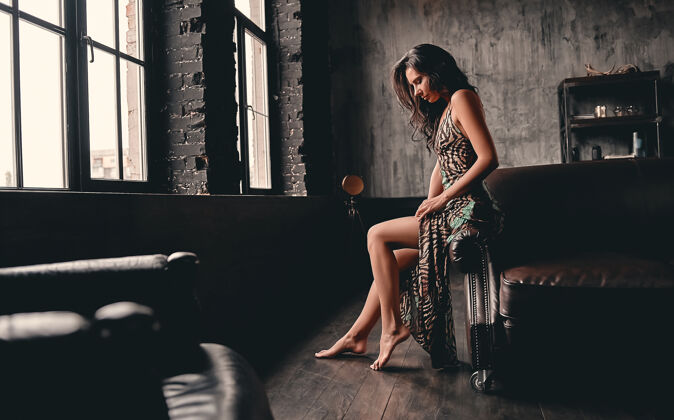 腿一个漂亮的黑发女人的肖像 卷发 穿着一件裙子 坐在皮沙发上摆姿势 露出修长的双腿身材女士精致
