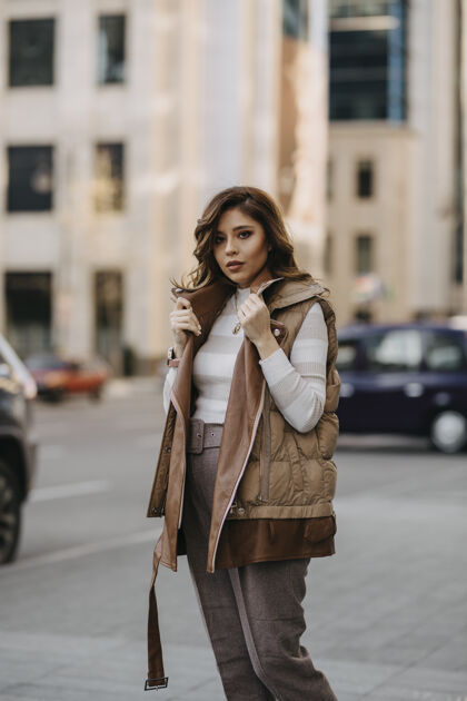 套头衫穿着冬装的漂亮女孩在街上 后面是建筑物和汽车 看前面时尚发型晴天街道