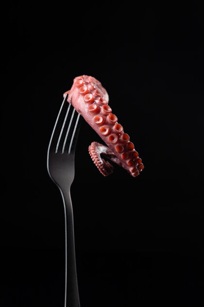 美食在黑暗的背景下用叉子抓住章鱼的触角没有身体烹饪食物