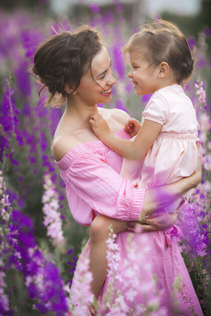 孩子年轻漂亮的妈妈和她的小女儿一起在户外玩耍花紫罗兰色花坛日落母性女孩