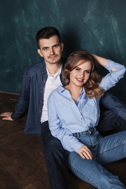 男人穿着牛仔裤的年轻人和女人一起坐在蓝色墙壁旁的木地板上微笑着关系女朋友情侣