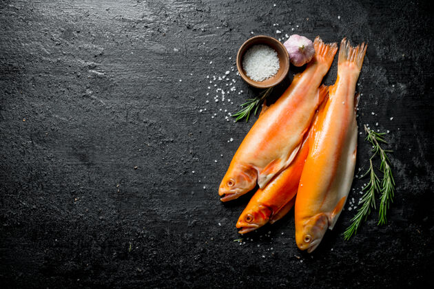 鱼黑木桌上有迷迭香 大蒜和盐的生鳟鱼鲑鱼海洋有机