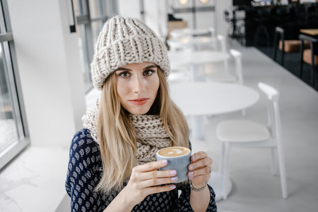 围巾美丽可爱的冬日女孩戴着针织帽子和手套喝着咖啡马克杯很吸引人以咖啡馆为背景的热饮女孩喝咖啡 享受生活柔软美丽热