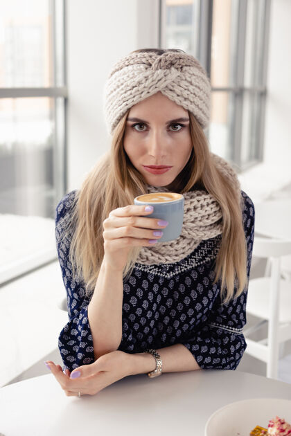 柔软美丽可爱的冬日女孩戴着针织帽子和手套喝着咖啡马克杯很吸引人以咖啡馆为背景的热饮女孩喝咖啡 享受生活羊毛拿铁咖啡可爱