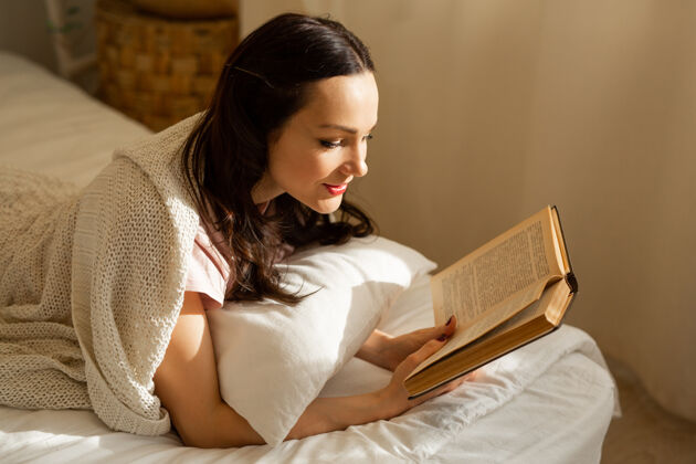 房子漂亮的年轻女子在卧室的床上拿着一本书早晨床微笑