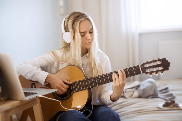 休闲美丽的年轻女子坐在床上弹吉他主页.肖像可爱的女孩音乐家吉他漂亮