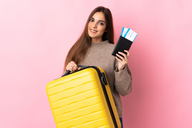 好年轻的白人妇女带着手提箱和护照在度假时被隔离在粉色背景下护照旅行粉色