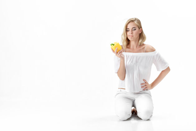 体重穿着白色上衣的漂亮严肃的金发女人看着黄色的铃铛胡椒粉健康吃和节食健康有机年轻