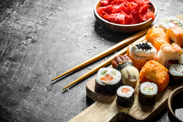 开胃菜不同种类的寿司 麦片和卷放在切菜板上 配以生姜和大豆沙司黑乡村的桌子寿司新鲜服务