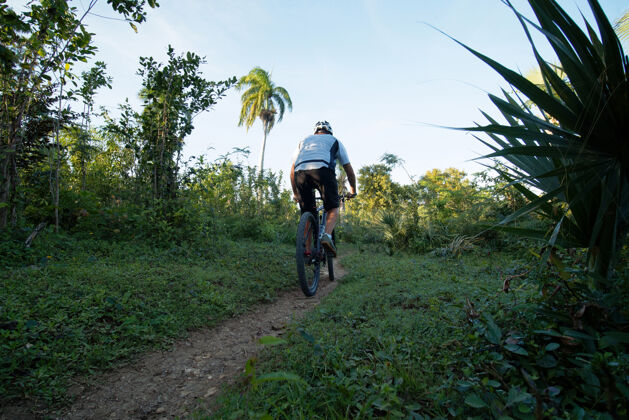人行道人骑山地车在热带自然 后视图健康人头盔
