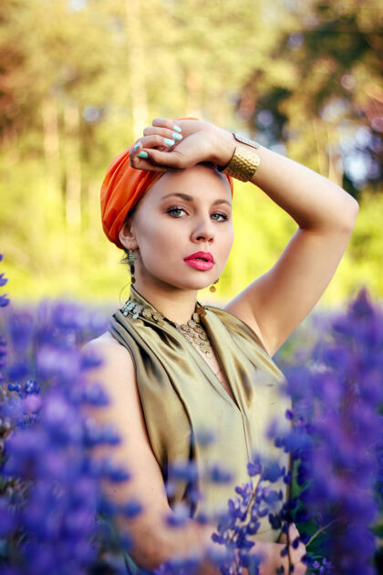 珠宝在羽扇豆地里 一个戴着橙色头巾的美丽女孩的画像自然美丽模糊