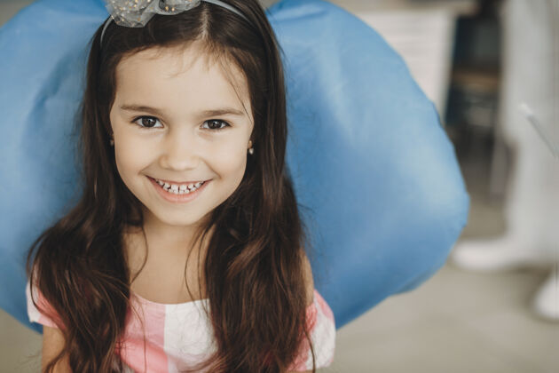 微笑一个可爱的小女孩坐在口腔科的座位上看着相机笑的特写照片美丽牙科初级